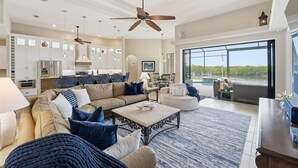 A spacious living area with a large sofa, coffee table, and dining table, a kitchen with modern appliances, and a view of a pool. - 90Degree Heated Pool/Spa - Nature Preserve SW Spreader Views (Cape Coral)