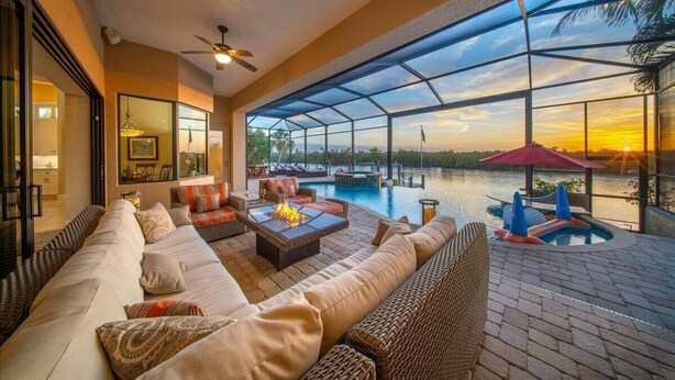 A spacious outdoor living area with a pool, comfortable seating, and a glass enclosure offering a view of the sunset. - 90Degree Heated Pool/Spa - Nature Preserve SW Spreader Views (Cape Coral)