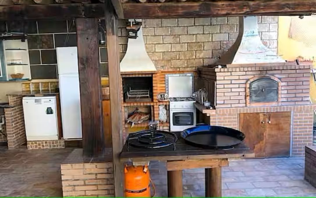 Ett utomhuskök med en tegelugn, en grill och ett kylskåp.