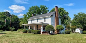 A two-story house with a brick chimney, white siding, and a covered porch. - Historic, private 3-bedroom house in Winston-Salem with ample parking. (Winston-Salem)
