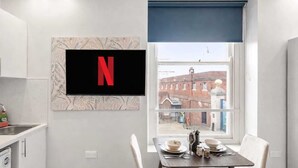 A modern kitchen with a flat-screen TV, a dining table with chairs, and a window with a view of buildings. - Modern Dockside Apartment | Near Gunwharf Quays (Portsmouth)