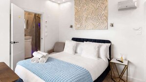 A hotel room with a bed, a bedside table, a wall-mounted air conditioner, and a door leading to a bathroom. - Modern Dockside Apartment | Near Gunwharf Quays (Portsmouth)