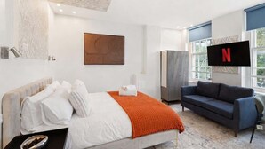 Ett modernt hotellrum med en säng, en soffa, ett stort fönster och en TV som är monterad på väggen.
