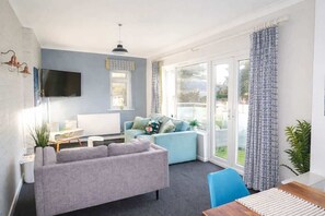 Ein modernes Wohnzimmer mit einem grauen Sofa, einem blauen Sessel, einem Holzesstisch und einem an der Wand befestigten Fernseher.