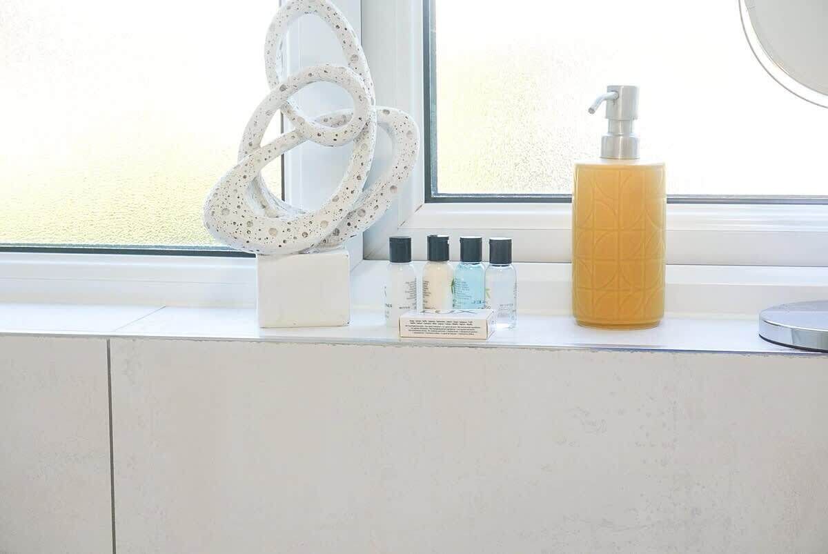 Een badkamermeubel met een raam, een witte handdoek, een flesje lotion en een set toiletartikelen.