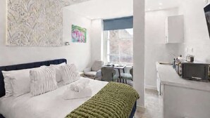 Een moderne hotelkamer met een bed, bureau, stoel, raam en kitchenette.