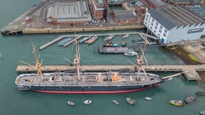 Een groot schip ligt aangemeerd in een haven, met diverse kleinere bootjes in de buurt.