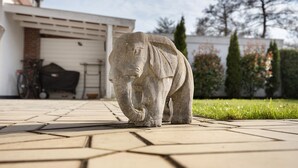 A stone elephant sculpture on a paved area with a garage and greenery in the background. - Holiday Home for 6 Guests, 150 m², in Winsen (Luhe) with Wi-Fi (Winsen (Luhe))