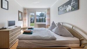 A bedroom with a bed, a dresser, a television, and a window with curtains. - Holiday Home for 6 Guests, 150 m², in Winsen (Luhe) with Wi-Fi (Winsen (Luhe))