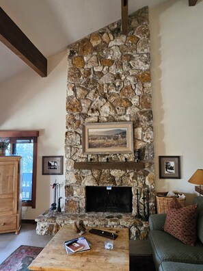 A stone fireplace with a framed picture above it, a wooden table with books and a candle, and a green sofa with a patterned pillow. - Brilliant 4BR/3BA Lake Tahoe Condo w/ Pool, Private Bouy, & Dock (Tahoe City)