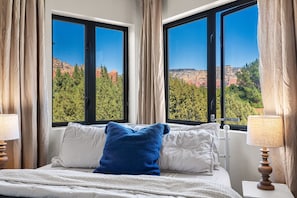 Ein Schlafzimmer mit einem Bett, zwei Nachttischlampen und einem Fenster mit Blick auf die Berge.