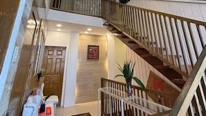 A multi-level interior with a staircase, a seating area with a white chair, and a patterned rug.