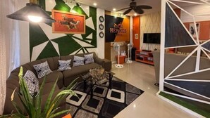 A modern living room with a sofa, decorative pillows, a floor lamp, a television, and a wall with geometric patterns.
