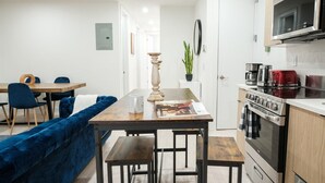 Eine moderne Küche mit Mikrowelle, Herd und Kaffeemaschine. Es gibt eine Essecke mit Tisch und Stühlen sowie ein blaues Sofa.