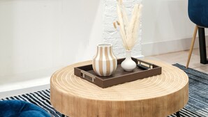 Ein runder Holztisch mit einer Ablage, auf der sich eine gestreifte Vase und eine weiße Vase mit Pampasgras befinden.