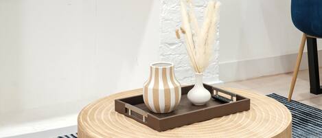A round wooden table with a tray holding a striped vase and a white vase with pampas grass.
