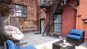 Eine Dachterrasse mit Korbmöbeln, einem Hängesessel und einer Leiter an einem Backsteinhaus.