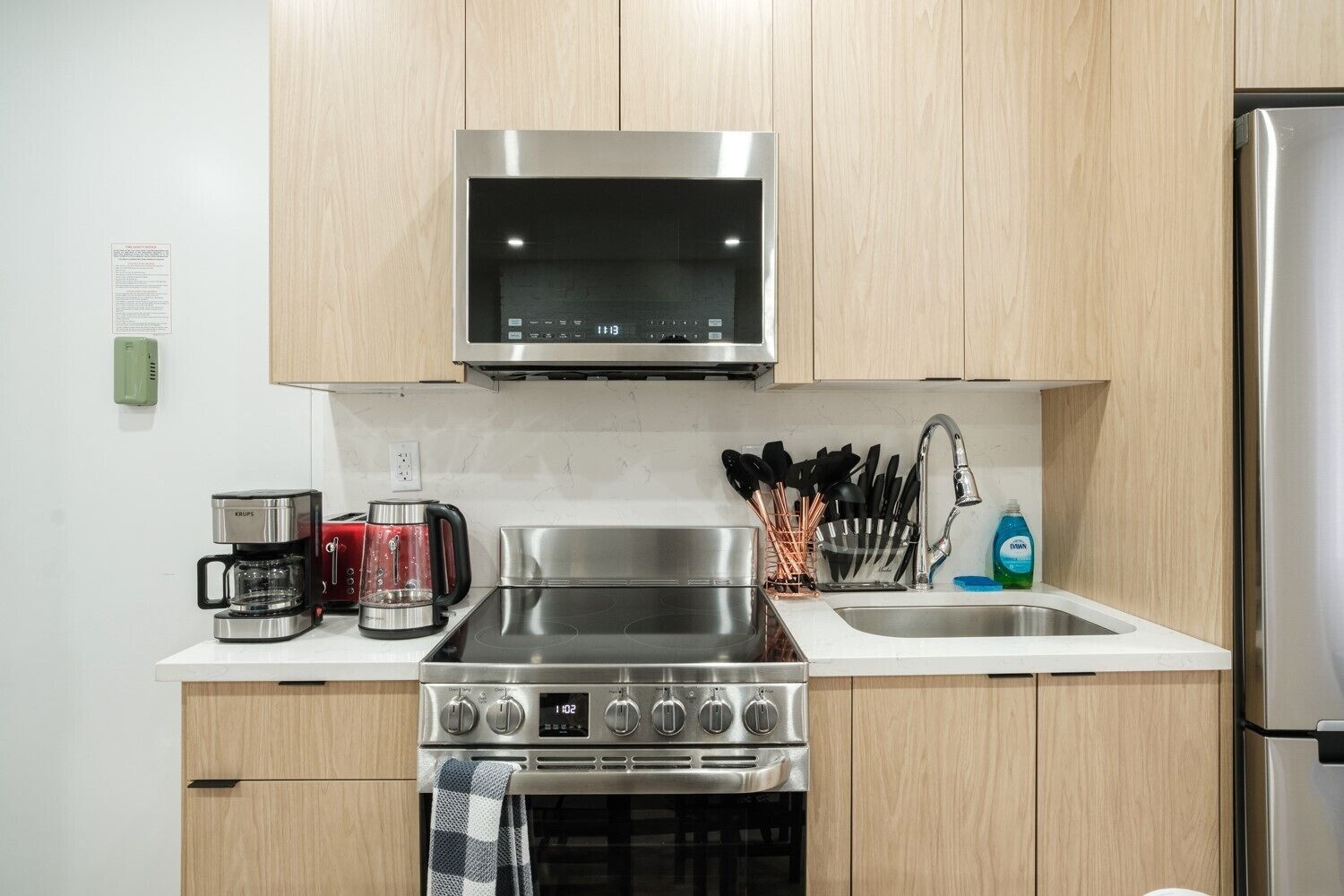 A modern kitchen with stainless steel appliances, wooden cabinets, a built-in microwave, and a coffee maker.