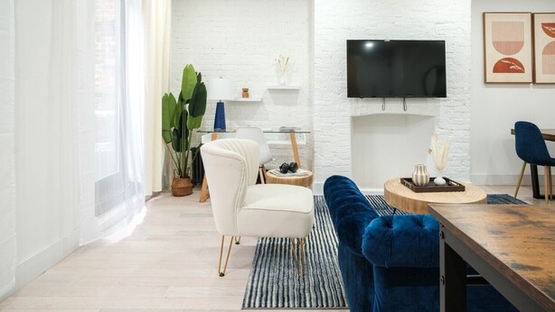 Ein modernes Wohnzimmer mit weißer Ziegelwand, Flachbildfernseher, einer Couch, einem Esstisch und einer großen Pflanze.