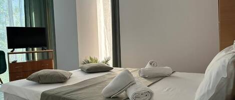 Quarto de hotel com cama, televisão, cômoda e janela com cortinas.