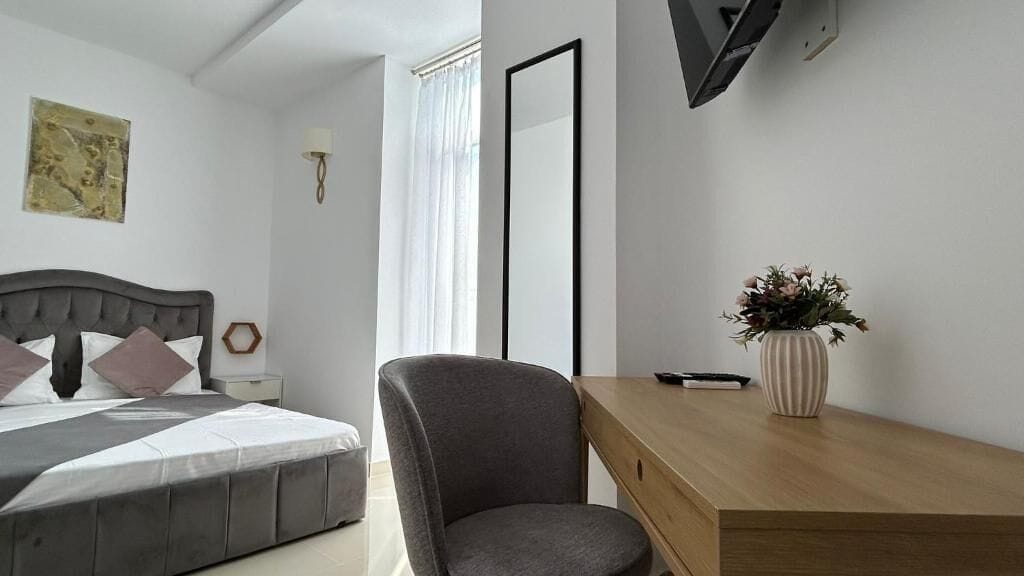 A modern bedroom with a bed, bedside table, chair, desk, and a potted plant.