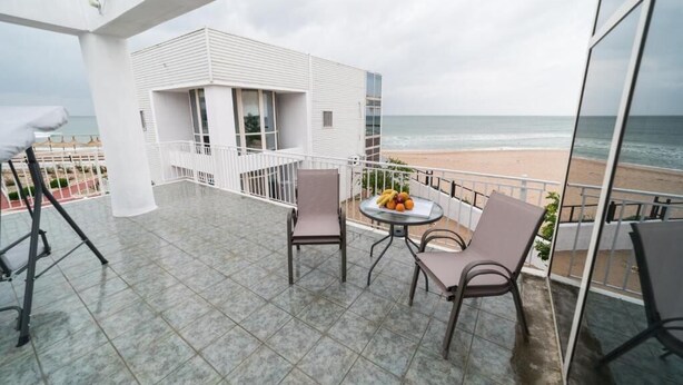 A balcony with a table and chairs, a white building, and a beach view. - Avenue Palm (Eforie Nord)