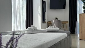 A modern hotel room with a large bed, a flat-screen TV mounted on the wall, and a wooden side table. - Avenue Palm (Eforie Nord)