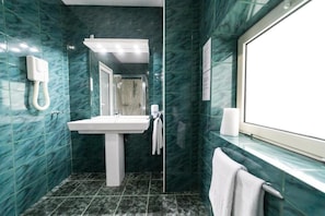 Une salle de bain avec un lavabo blanc, un miroir, une cabine de douche et une fenêtre.