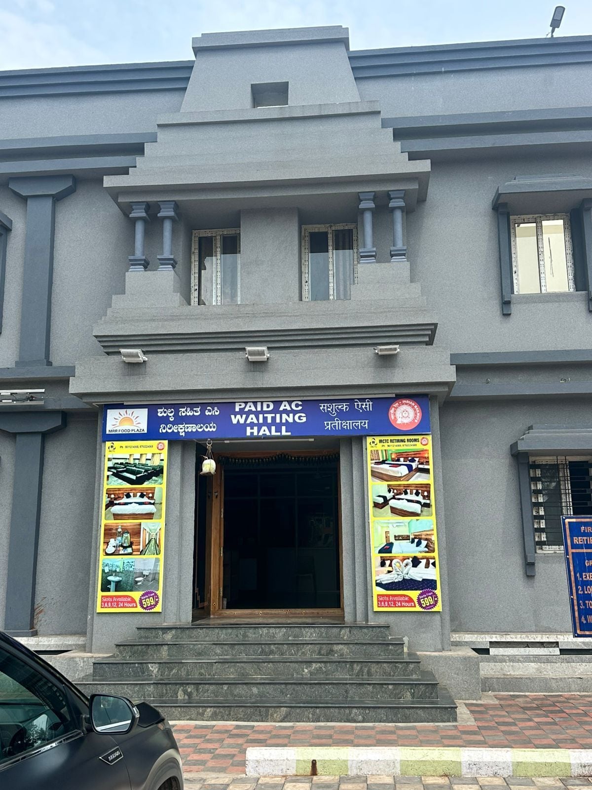 Um edifício com o letreiro 'PAID AC WAITING HALL', degraus que levam à entrada e um carro estacionado.