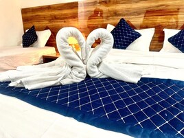 Una cama con colcha azul y almohadas, cabecero de madera, y una toalla dispuesta en forma de corazón.