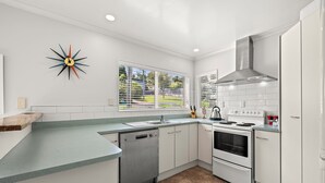 Eine moderne Küche mit weißen Schränken, einem Edelstahl-Geschirrspüler, einem Backofen mit zwei Garstufen und einem Fenster mit Jalousien.
