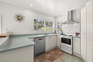 Eine moderne Küche mit weißen Schränken, einem Edelstahl-Geschirrspüler, einem Backofen mit zwei Garstufen und einem Fenster mit Jalousien.