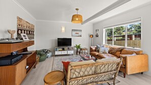 Ein Wohnzimmer mit einer Couch, einem Fernseher, einem Holzschrank und einem großen Fenster.