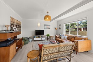 Ein Wohnzimmer mit einer Couch, einem Fernseher, einem Holzschrank und einem großen Fenster.
