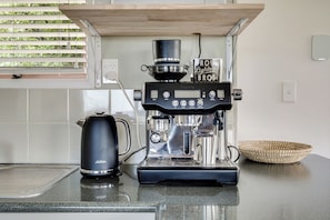 Une machine à café, une bouilloire et un panier en osier sur un plan de travail de cuisine.