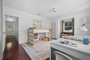 Ein Schlafzimmer mit Etagenbett, Schreibtisch mit Lampe, Fenster mit Rollläden und gerahmten Bildern an der Wand.