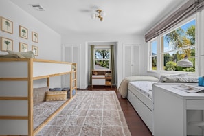 Ein Schlafzimmer mit Etagenbett, Schreibtisch mit Lampe, Fenster mit Vorhängen und gerahmten Pflanzenbildern an der Wand.