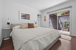 Ein Schlafzimmer mit Bett, Nachttischen, einer Tür, die auf einen Balkon führt, und einem gerahmten Bild an der Wand.
