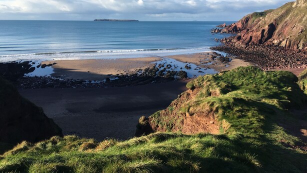 A coastal landscape with a beach, rocky cliffs, and a distant island. - Spacious Seaside Cottage in Dale, Pembrokeshire – Steps from the Beach, Sleeps 9 (Haverfordwest)