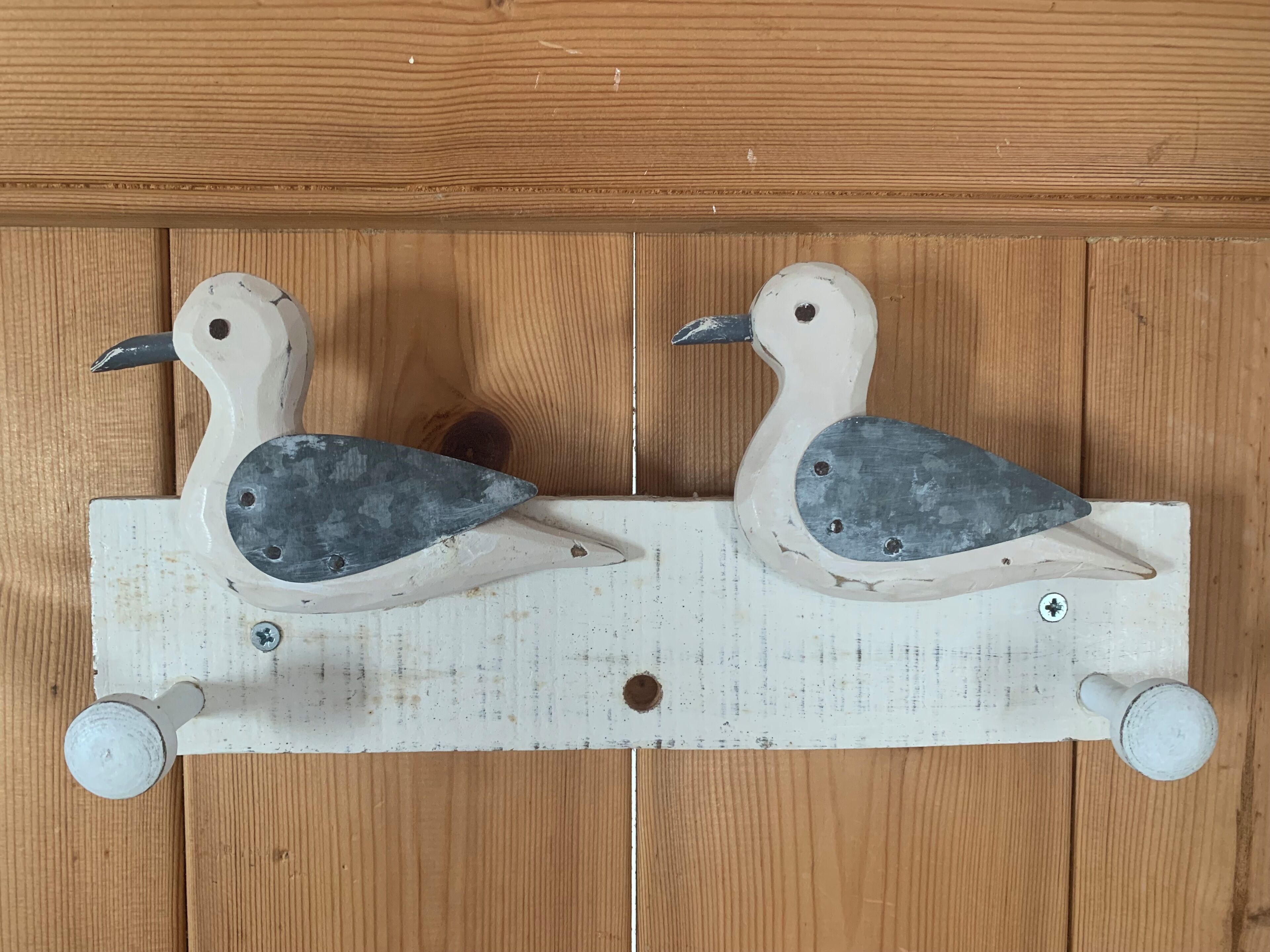 Two wooden bird-shaped objects mounted on a white board with screws, set against a wooden background.