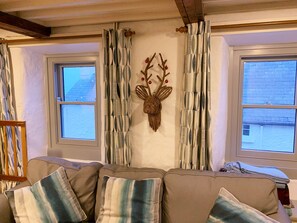 Ein Wohnzimmer mit einer Couch, gemusterten Vorhängen, einem Wandbild eines Hirschschädels und Fenstern mit Blick ins Freie.