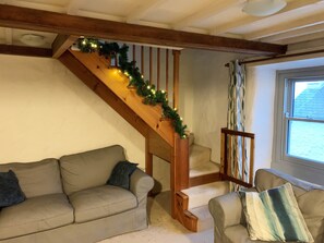 Eine Treppe mit Holzgeländern und einer Girlande, ein beiges Sofa und ein Sessel mit Kissen.