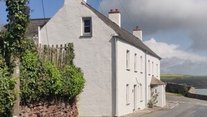 A white building with a stone wall and a wooden fence, a clear sky, and a view of the sea. - Spacious Seaside Cottage in Dale, Pembrokeshire – Steps from the Beach, Sleeps 9 (Haverfordwest)