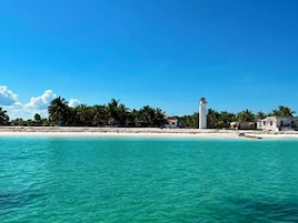 Paesaggio costiero con un faro, spiaggia e palme.