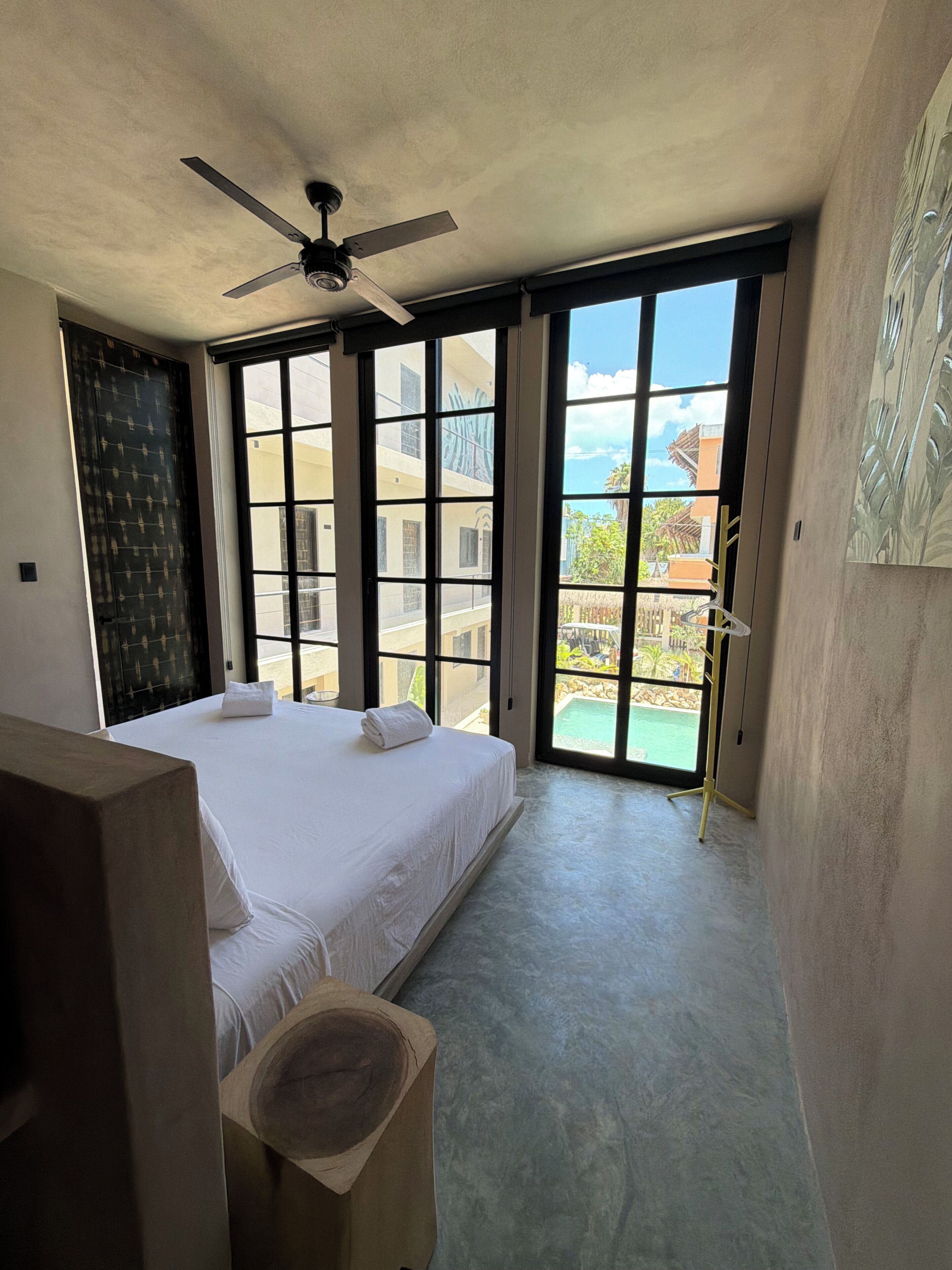 Ein Schlafzimmer mit einem großen Bett, einem Deckenventilator und Blick auf einen Pool sowie Gebäude im Freien.