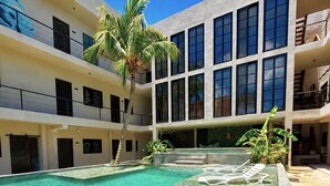 Un edificio de varios niveles con piscina central, palmeras y cielo azul despejado.