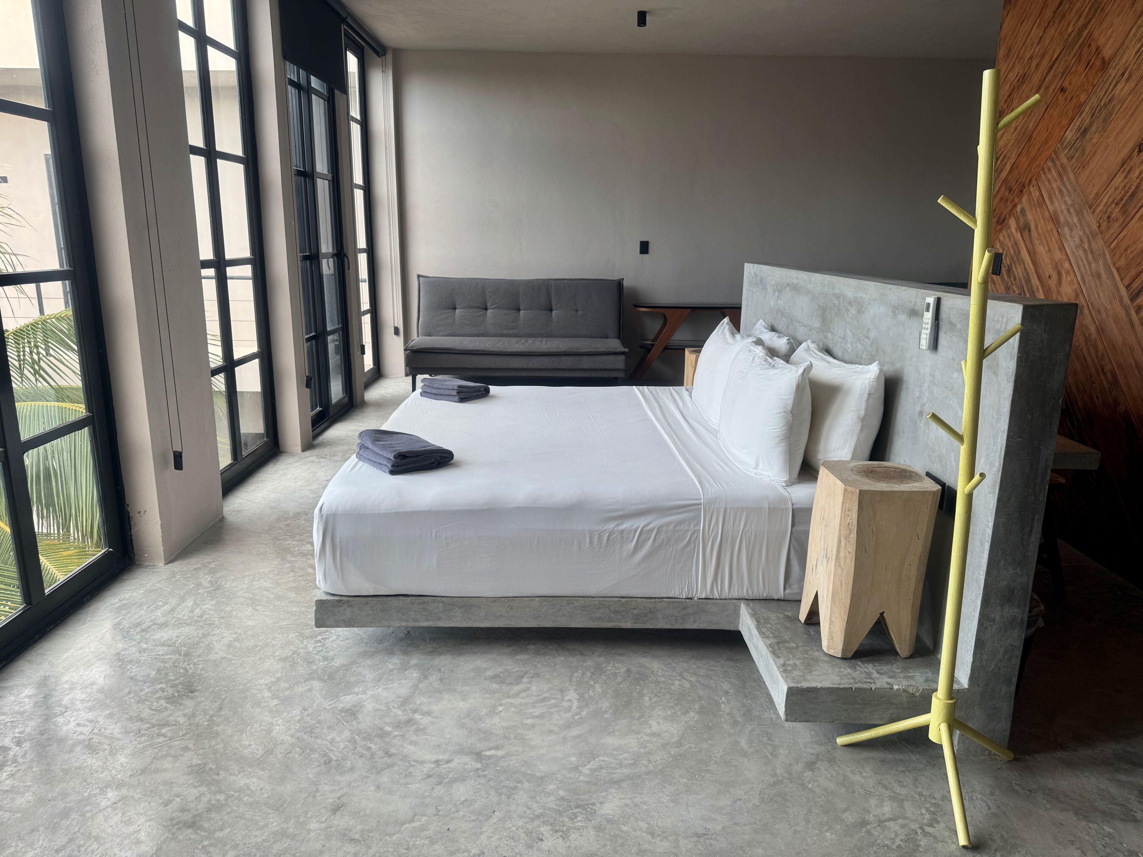 A modern bedroom with a large bed, a grey headboard, a bedside table, and a wooden wall.