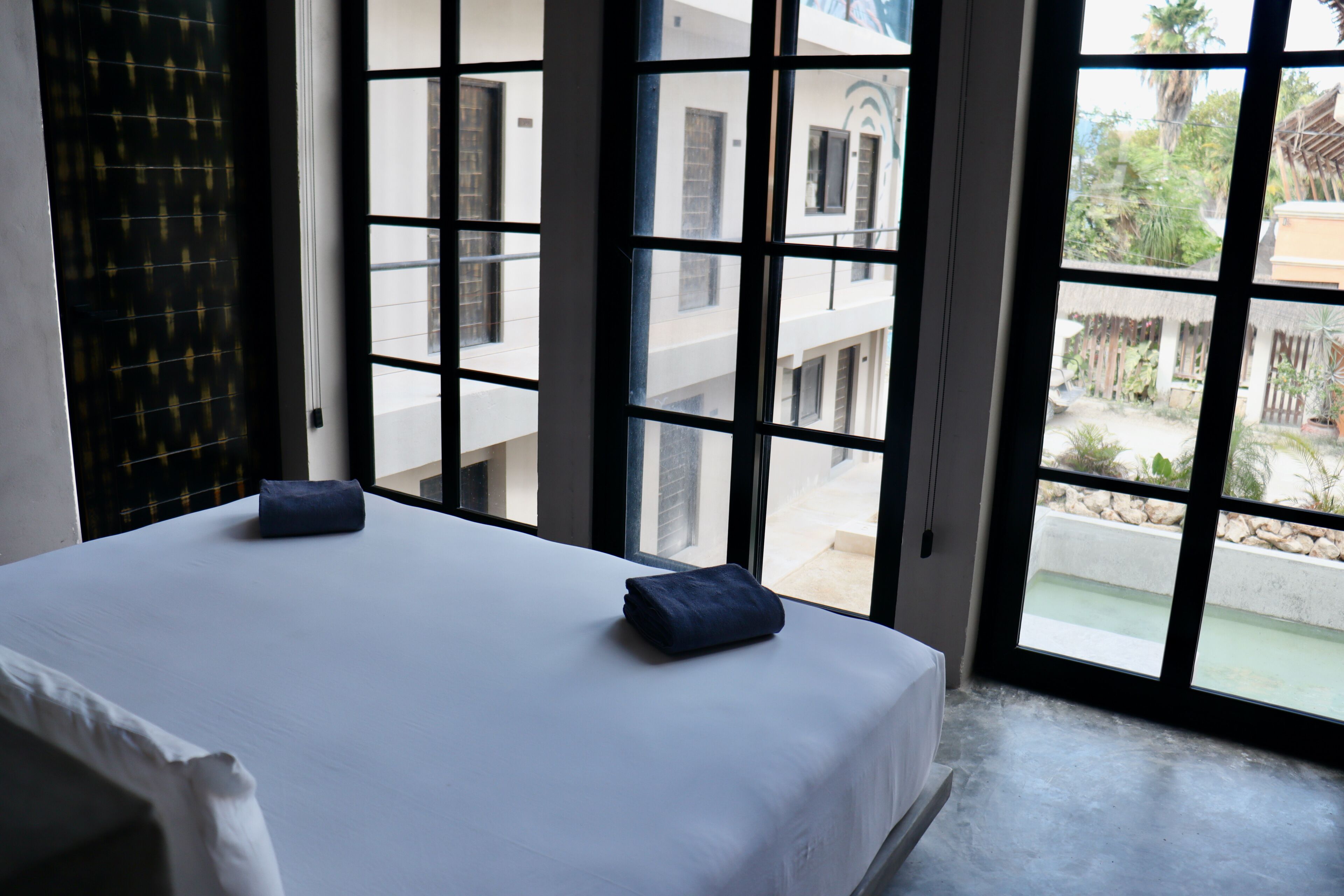Ein Hotelzimmer mit Bett, zwei Kissen und Blick durch große Fenster.