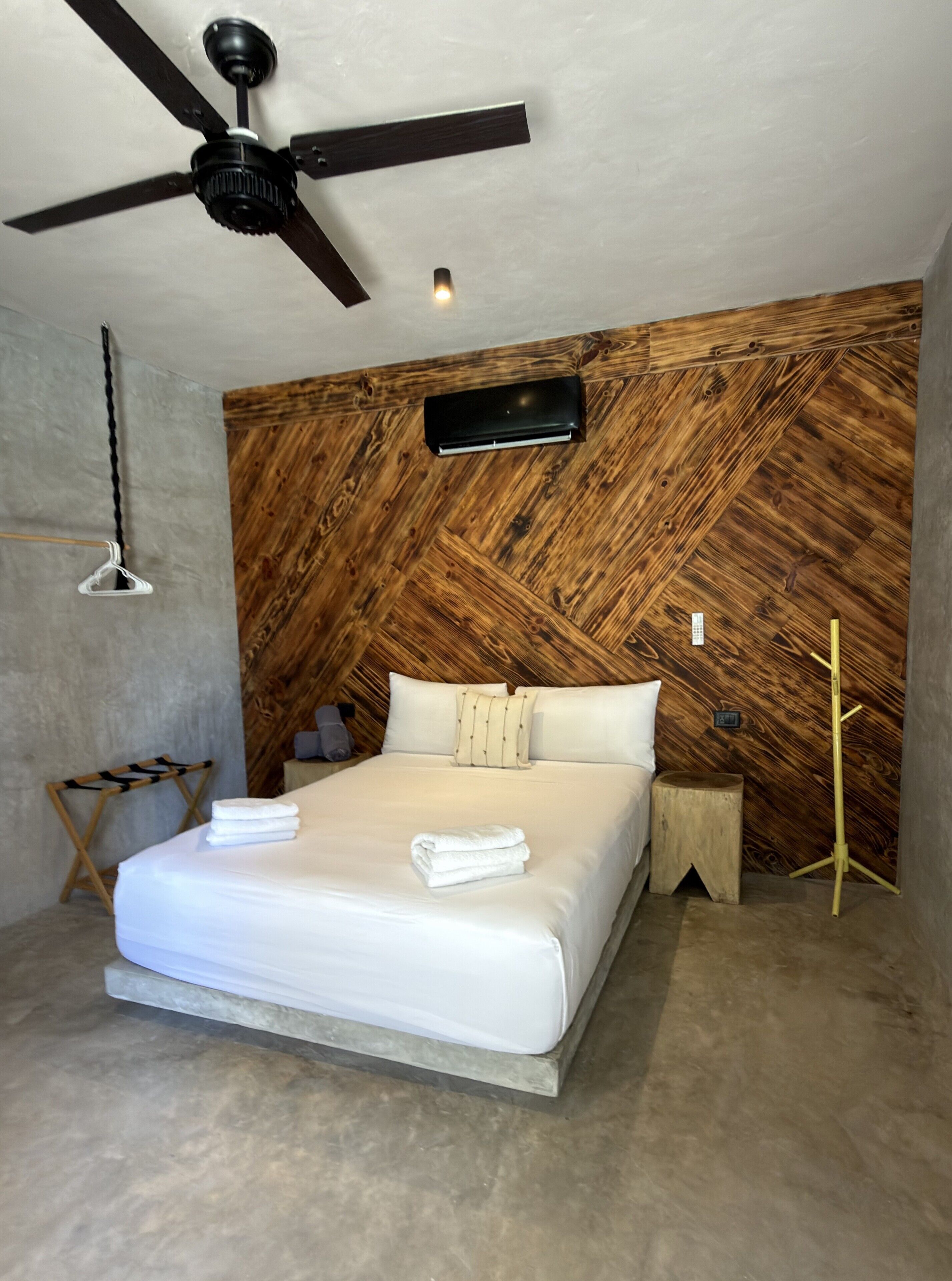 Un dormitorio moderno con cabecera de madera, ventilador de techo, mesita de noche y lámpara de noche.