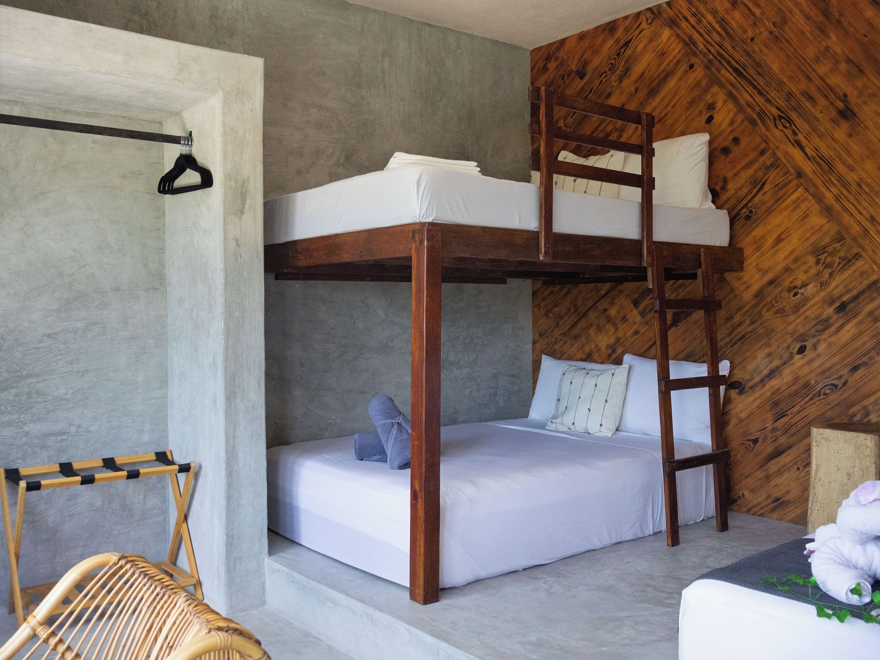 A bunk bed room with a wooden ladder, a hanging rack, and a wicker chair.